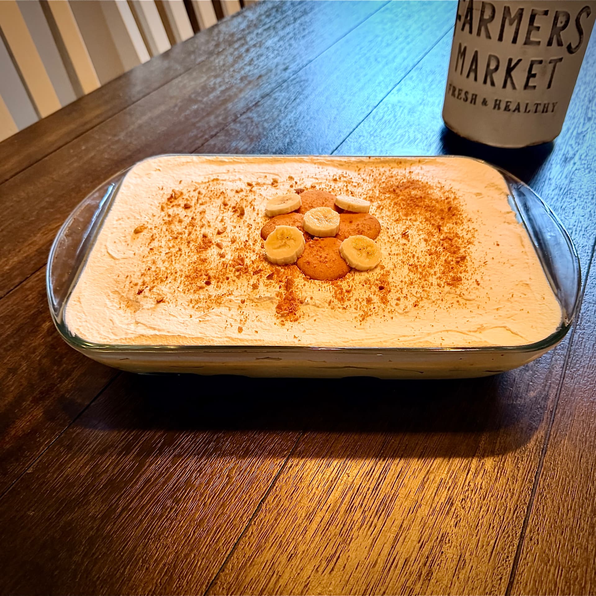 Close-up of No-Bake Nanner Puddin' in a glass dish topped with whipped cream, Nilla Wafers, banana slices, and cinnamon