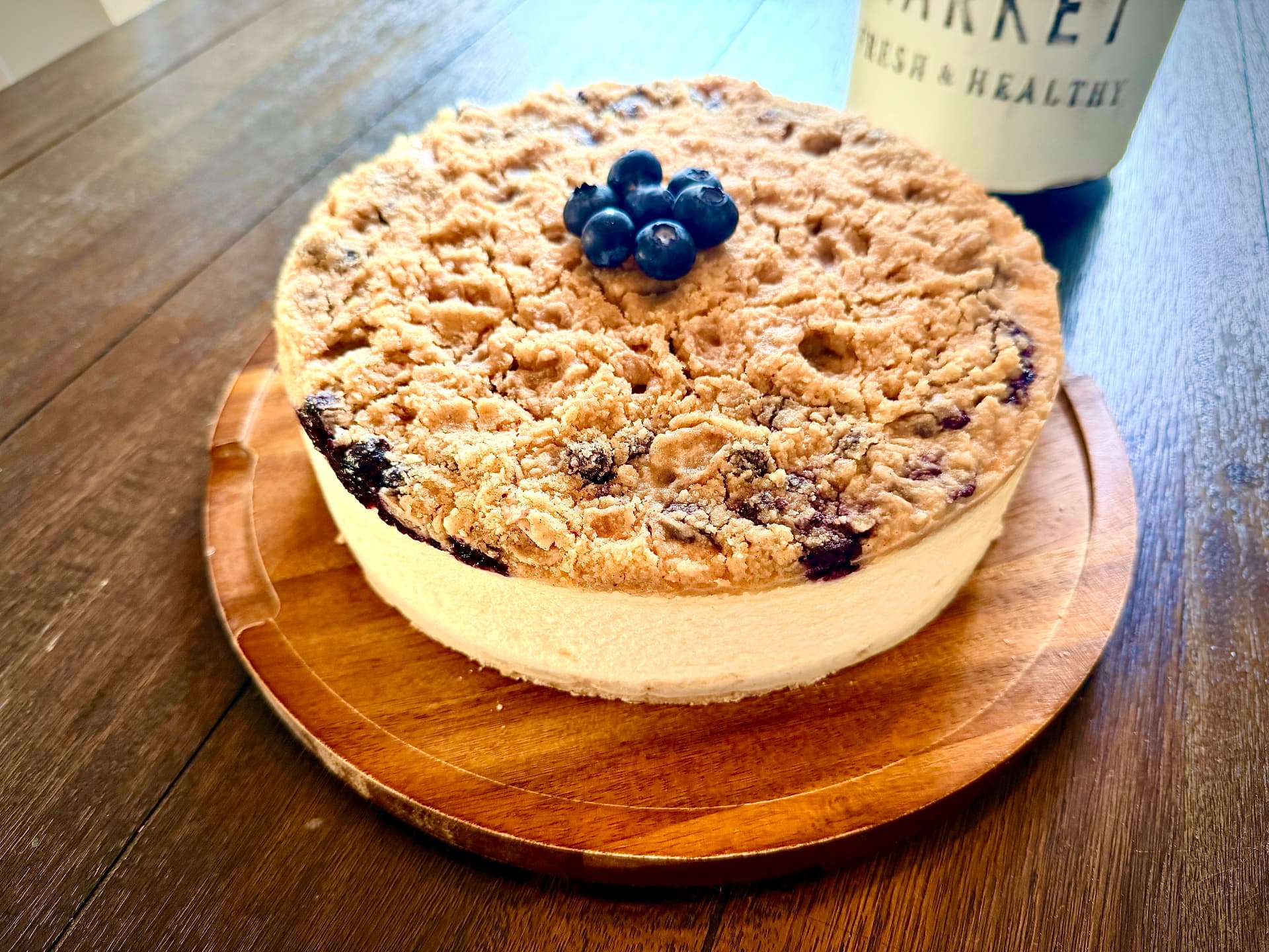 Close-up of Blueberry Muffin Cheesecake with golden streusel topping and fresh blueberries on a wooden board