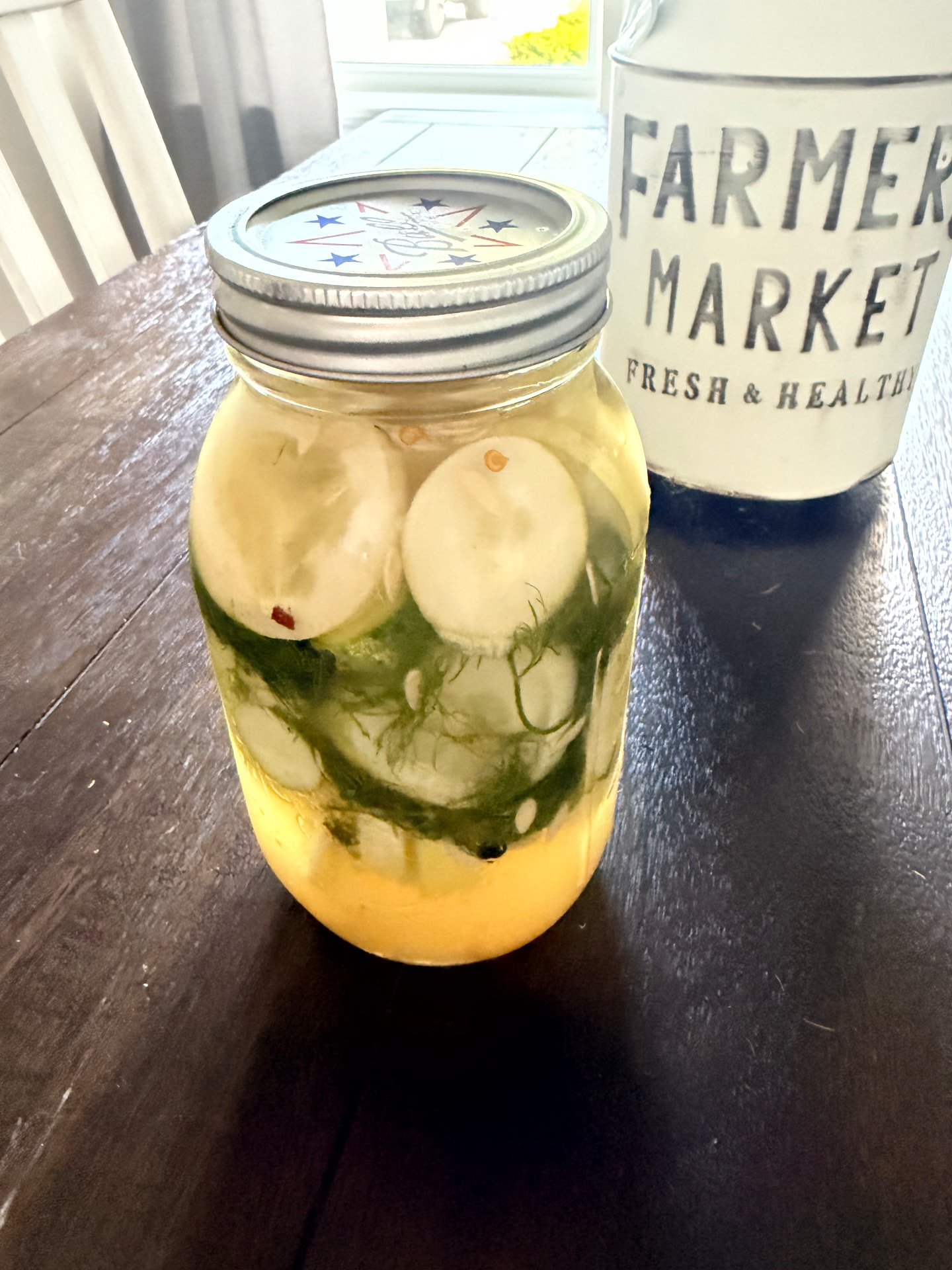 Close-up of a quart jar of classic refrigerator dill pickles with fresh dill, garlic, and peppercorns in the brine