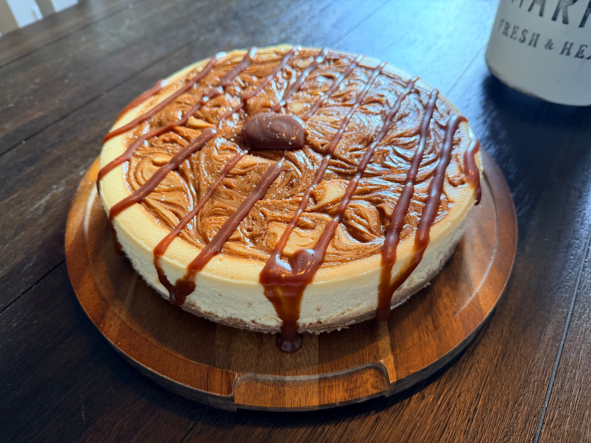 Close-up of Salted Caramel Cheesecake with swirled caramel top and crosshatch caramel drizzle on a wooden board